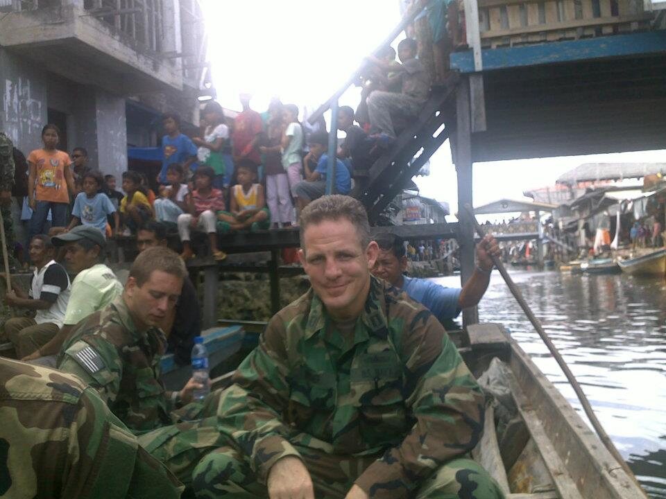 Grant in uniform smiling from a small boat in a stilt-village waterway in Sitankai, Philippines